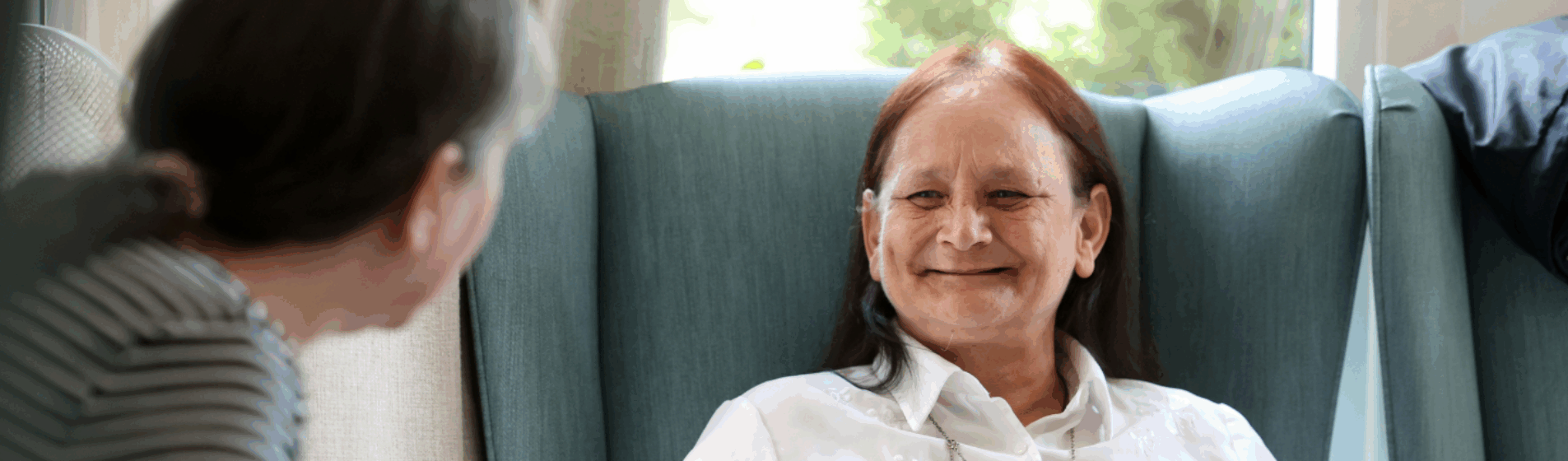 Care home resident smiling whilst sitting in the lounge and talking to another resident